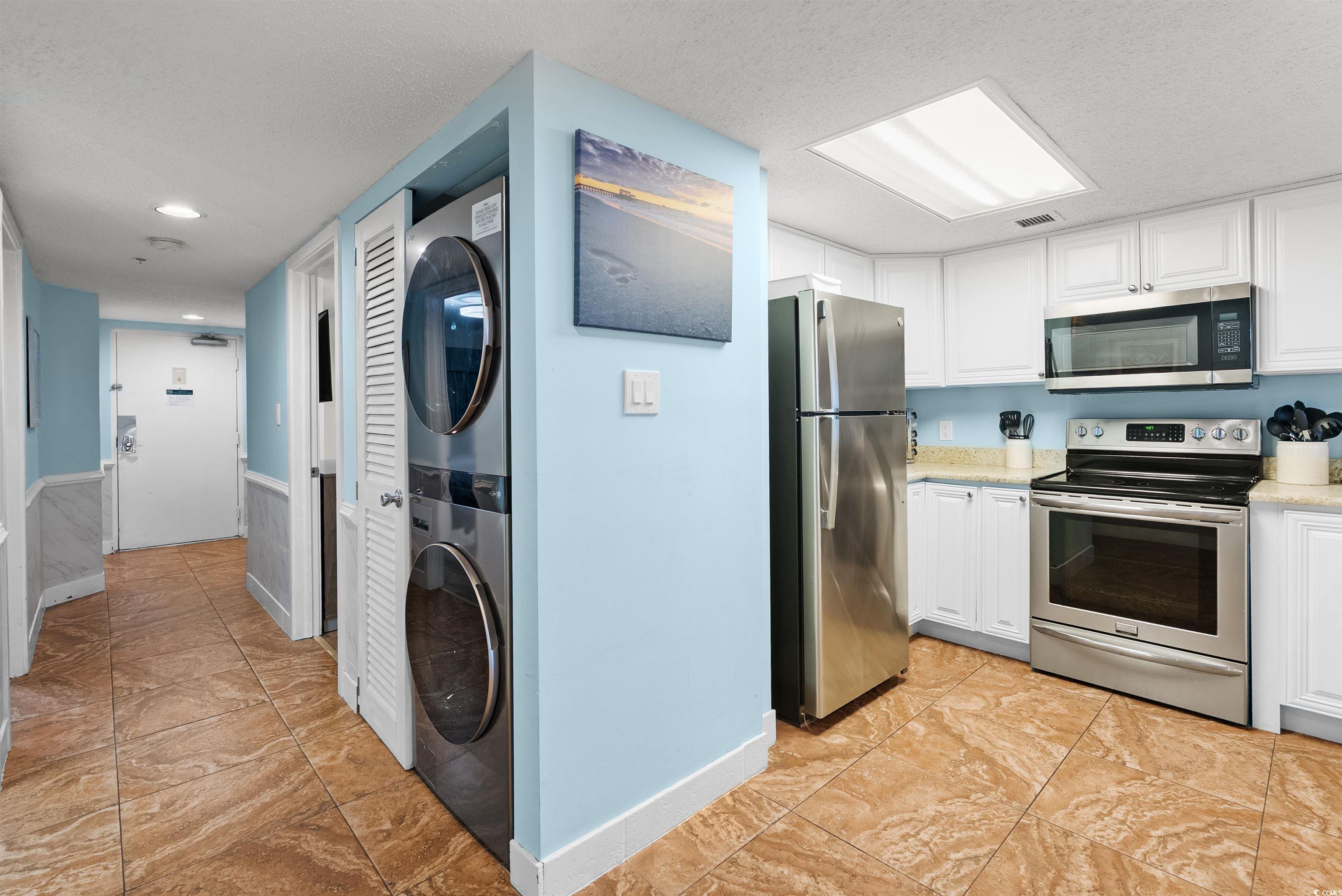 205 74th Avenue North, Unit 1908 Myrtle Beach, SC 29572 - Photo 10 of 39 Kitchen with white cabinetry, appliances with stainless steel finishes, stacked washer / drying machine, a textured ceiling, and light stone counters