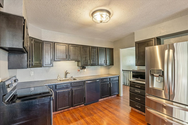 11 South Clark Lane Elk Ridge, UT 84651 - Photo 10 of 46 Kitchen featuring stainless steel appliances, dark wood finish cabinets, a textured ceiling, light wood finished floors, and light countertops