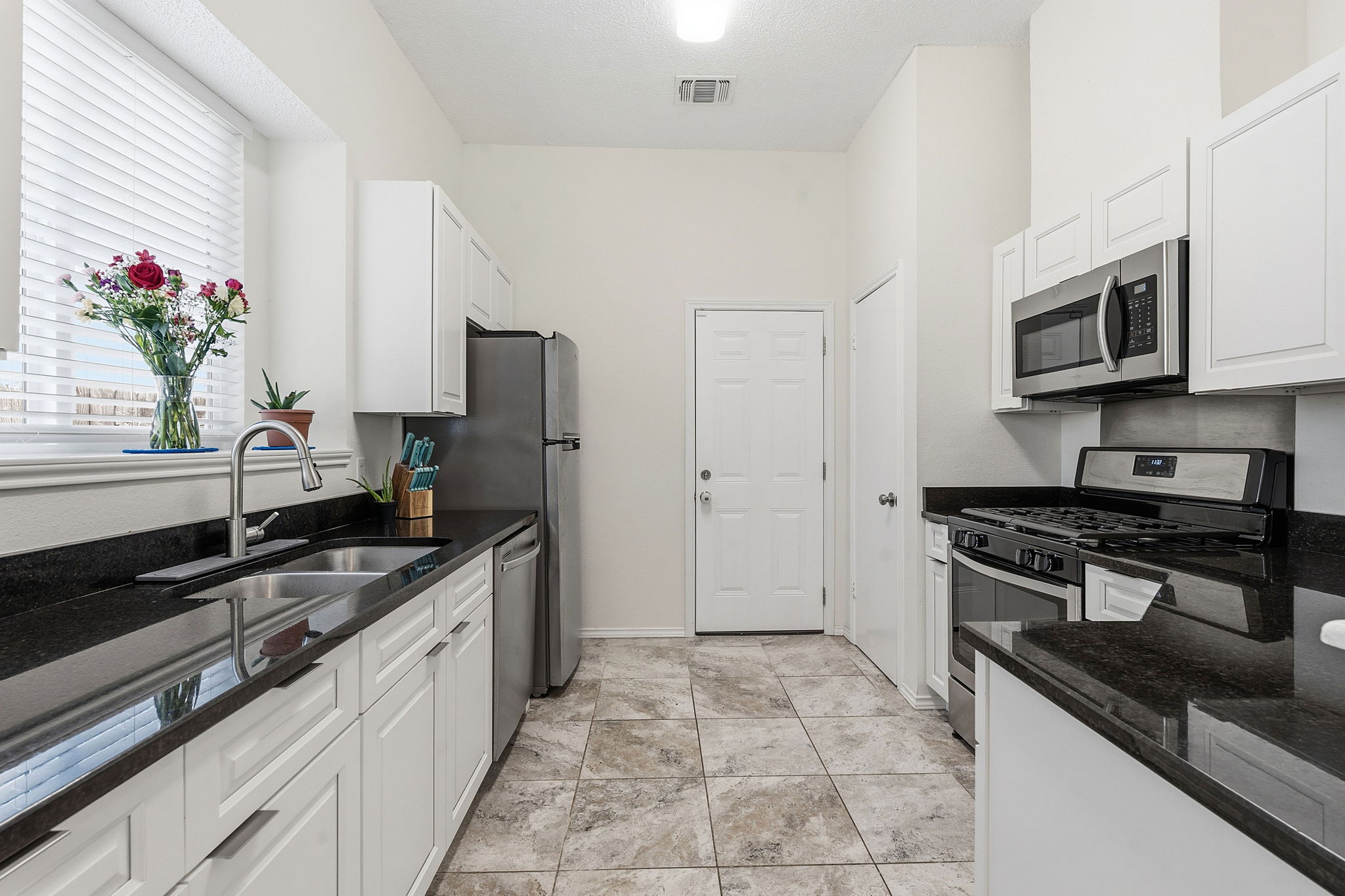 14818 Yellowleaf Trail Austin, TX 78728 - Photo 8 of 26 Kitchen featuring dark countertops, white cabinetry with silver hardware, stainless steel appliances, and tile flooring