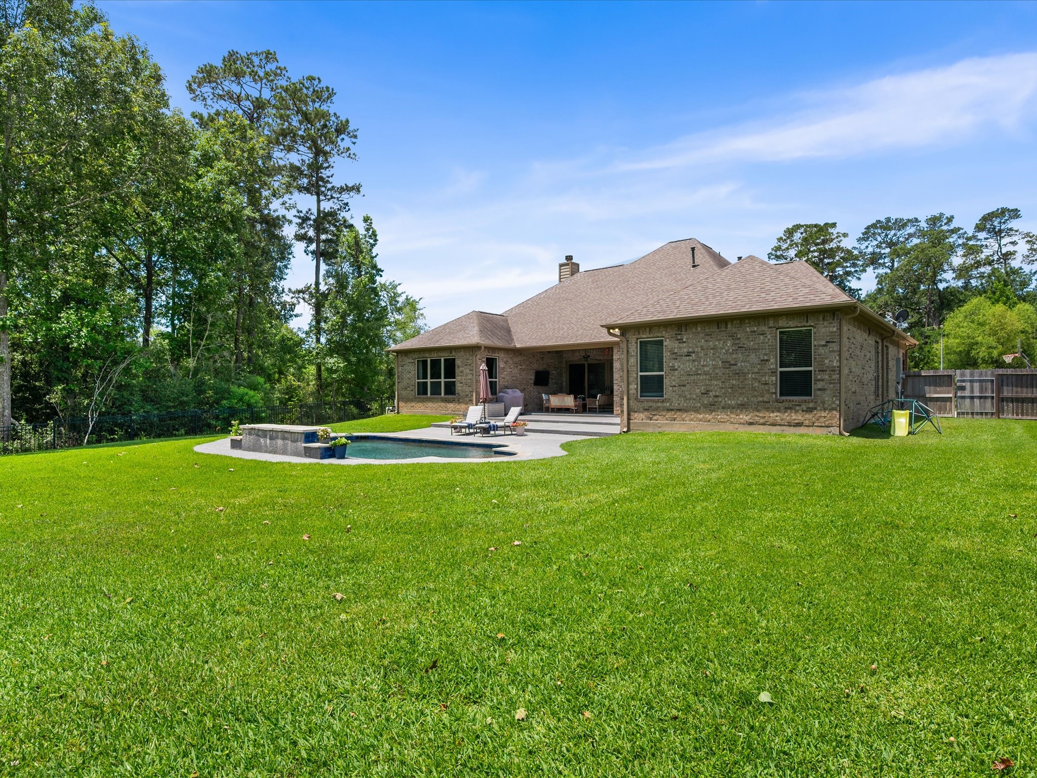 12618 Ranger Court Magnolia, TX 77354 - Photo 39 of 45 An expansive view of the sprawling, fully fenced backyard, showcasing the back of the brick home, an extended concrete patio, and a sparkling in-ground pool surrounded by a manicured, lush green lawn.