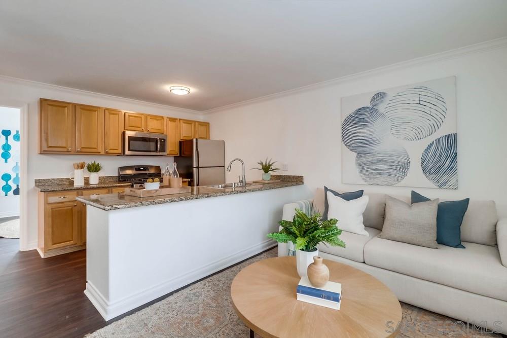 a living room with stainless steel appliances furniture a potted plant and a kitchen view