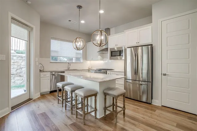 a kitchen with stainless steel appliances granite countertop a refrigerator a microwave a stove and white cabinets with wooden floor