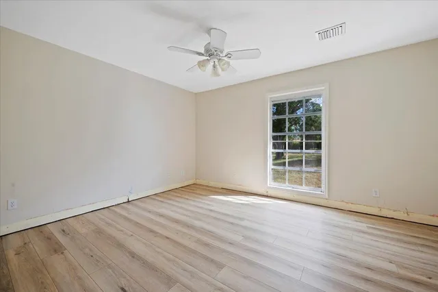 an empty room with wooden floor fan and windows
