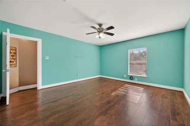 an empty room with wooden floor chandelier fan and windows