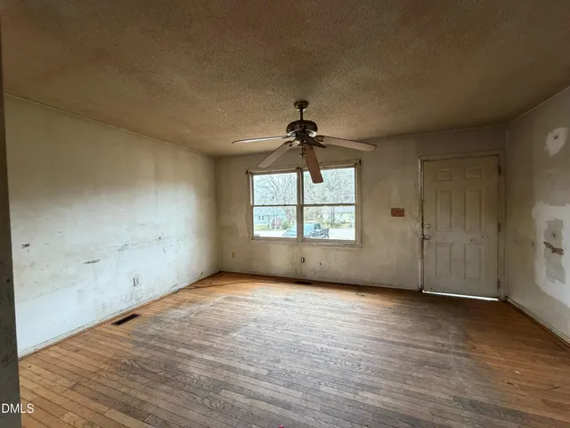 an empty room with wooden floor chandelier fan and windows