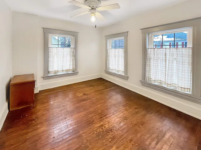 an empty room with wooden floor fan and windows