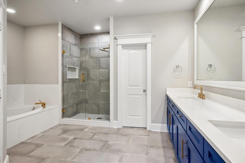 1600 Abrams Road, Unit 38 Dallas, TX 75214 - Photo 10 of 17 Spacious bathroom featuring a frameless glass shower enclosure with large format tile, a deep soaking tub with deck-mounted fixtures, and a dual vanity with white countertops and blue cabinetry