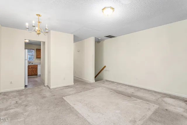 an empty room with chandelier fan and refrigerator