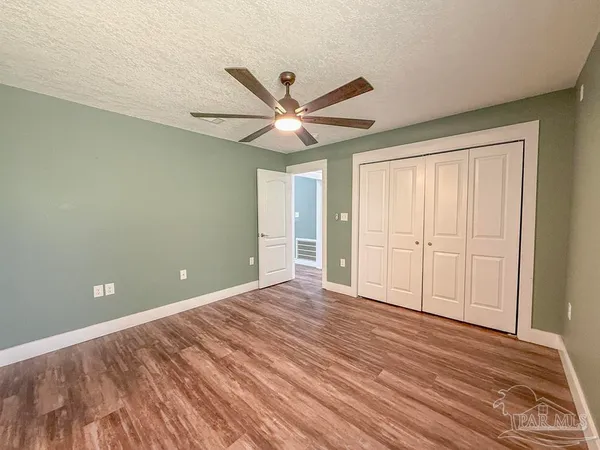an empty room with wooden floor chandelier fan and windows
