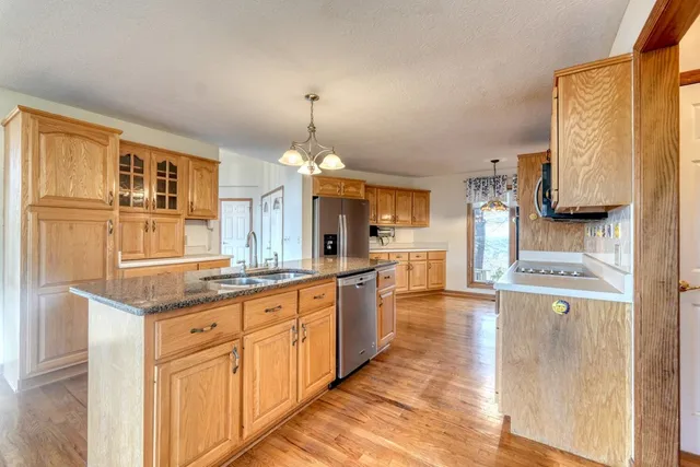 a open kitchen with granite countertop a stove top oven a sink dishwasher and cabinets with wooden floor