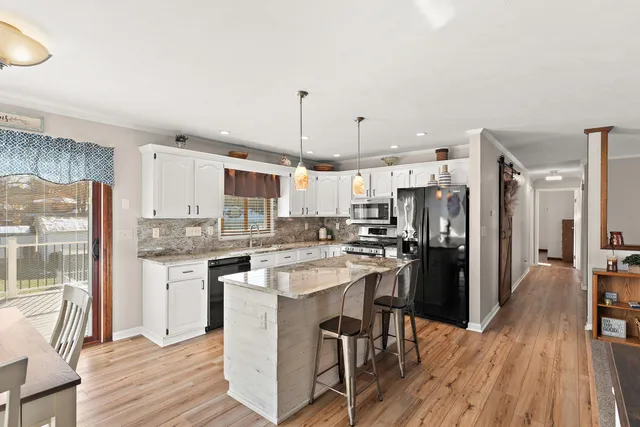 a kitchen with stainless steel appliances kitchen island granite countertop a refrigerator a stove a sink a dining table and chairs with wooden floor