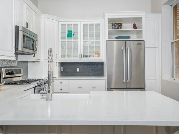 a living room with stainless steel appliances a couch a flat screen tv and a window
