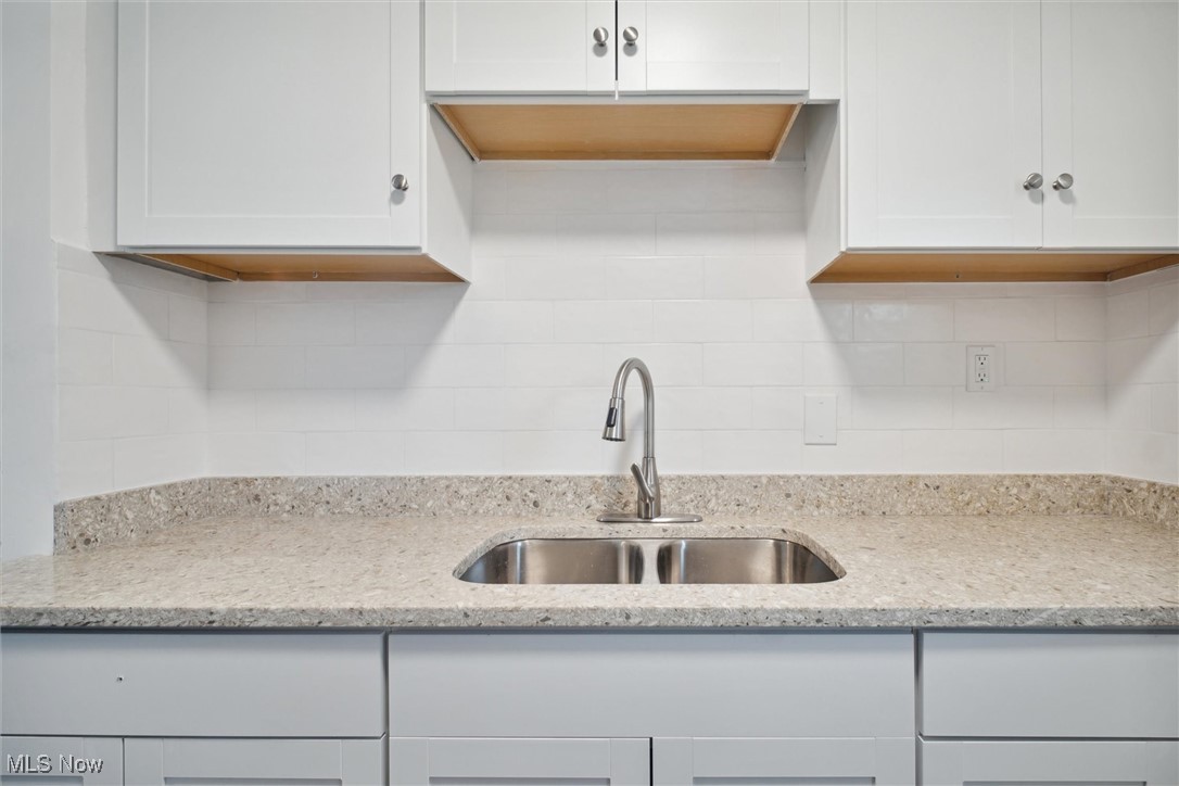 8796 West Ridgewood Drive Cleveland, OH 44130 - Photo 17 of 38 Kitchen with light stone counters, sink, decorative backsplash, and white cabinetry