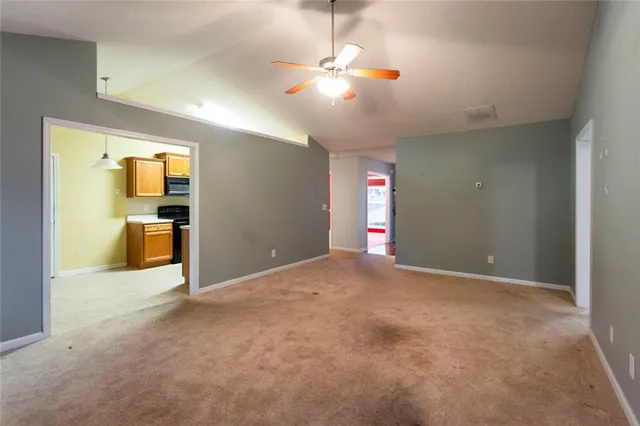 an empty room with fan and way to kitchen