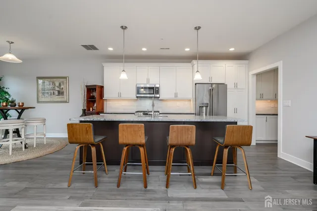 a kitchen with stainless steel appliances granite countertop a dining table chairs refrigerator and sink