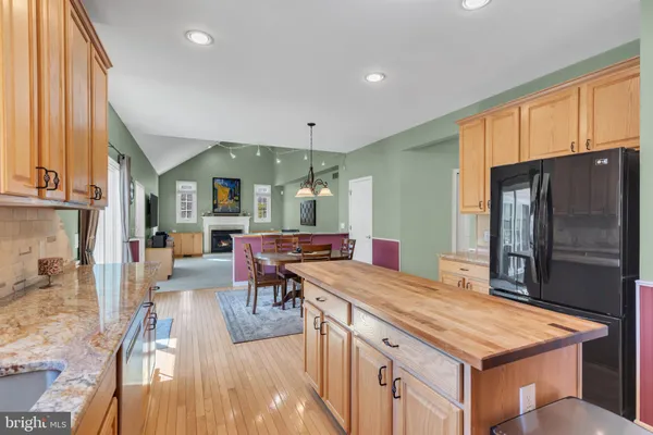 a kitchen with stainless steel appliances granite countertop a refrigerator a sink dishwasher a stove and a dining table with wooden floor