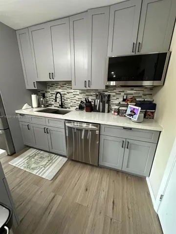 a kitchen with stainless steel appliances a stove top oven a sink dishwasher and white cabinets with wooden floor