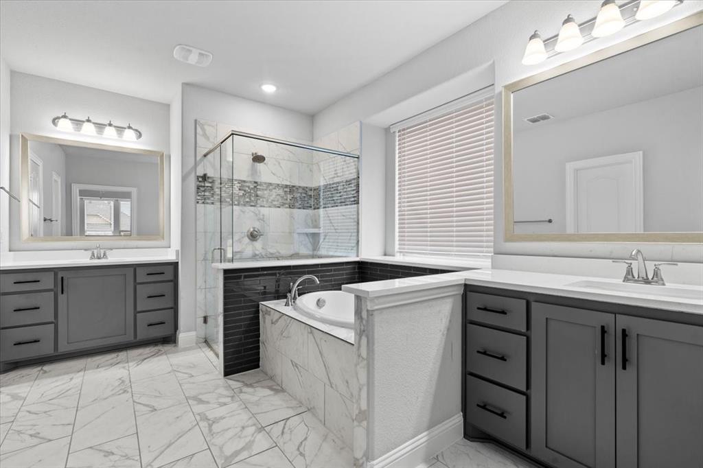 620 Shadow Trail Frisco, TX 75033 - Photo 18 of 36 Spacious bathroom featuring a built-in soaking tub, a glass-enclosed shower, dual vanity sinks with dark cabinetry, large framed mirrors, and marble-look floor tiling
