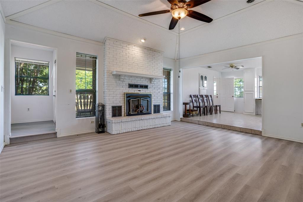 7397 Fm 1377 Blue Ridge, TX 75424 - Photo 8 of 27 an empty room with wooden floor a fireplace a ceiling fan and windows