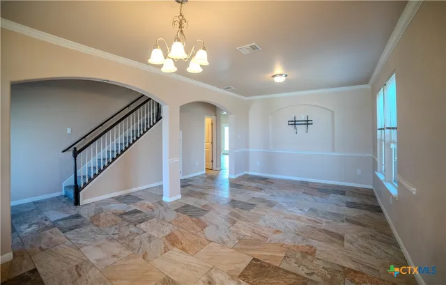a view of an empty room with stairs and a chandelier