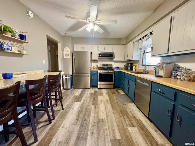 a kitchen with stainless steel appliances granite countertop a refrigerator a sink dishwasher a stove a dining table and chairs with wooden floor