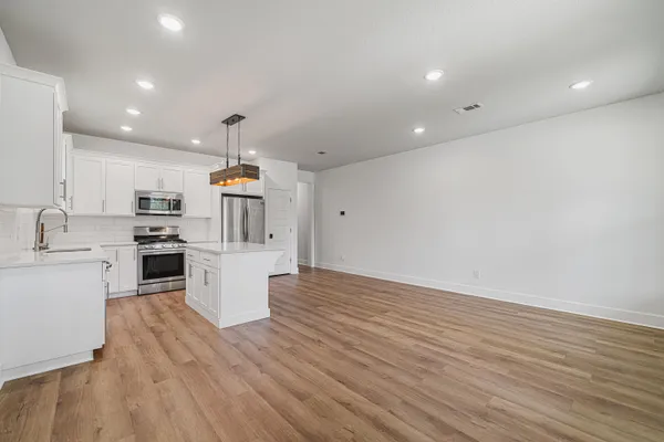 a kitchen with stove a refrigerator and white cabinets with wooden floor