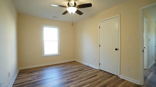 a view of empty room with wooden floor and fan