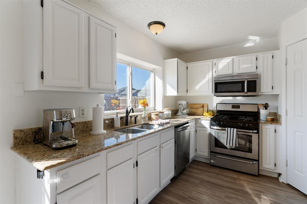 7518 Bayview Drive Rowlett, TX 75088 - Photo 8 of 22 Kitchen featuring stainless steel appliances, white cabinets, light stone counters, a textured ceiling, and dark wood finished floors