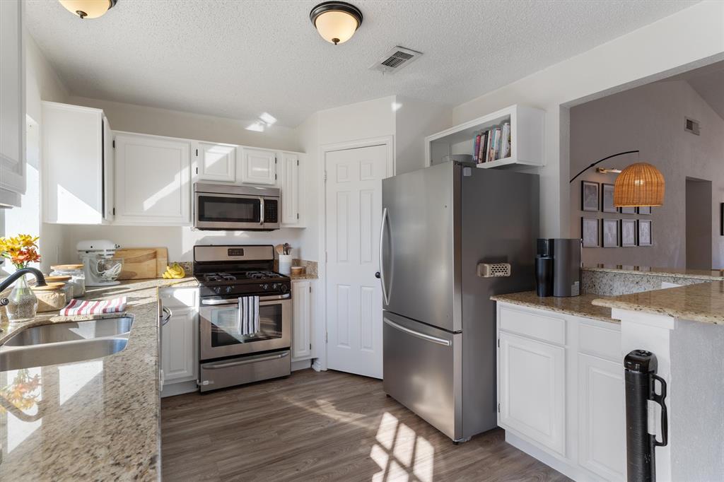 7518 Bayview Drive Rowlett, TX 75088 - Photo 9 of 22 Kitchen with white cabinetry, light stone countertops, stainless steel appliances, dark wood-style flooring, and a textured ceiling