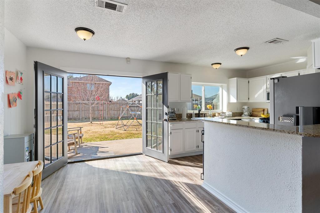7518 Bayview Drive Rowlett, TX 75088 - Photo 10 of 22 Kitchen featuring light stone countertops, white cabinets, light wood-type flooring, stainless steel refrigerator with ice dispenser, and a textured ceiling