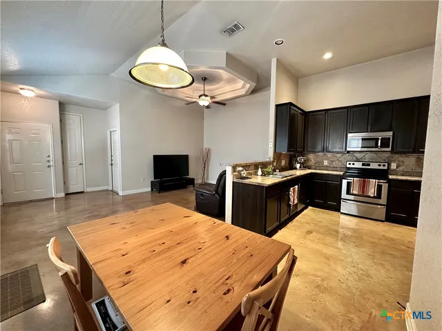 a kitchen with stainless steel appliances granite countertop a stove top oven a sink a refrigerator with a dining table and chairs