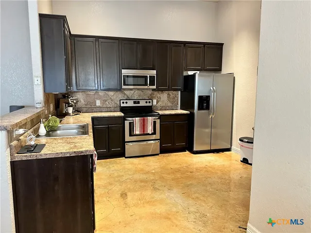 a kitchen with stainless steel appliances a sink a stove a microwave a refrigerator a counter top space and cabinets