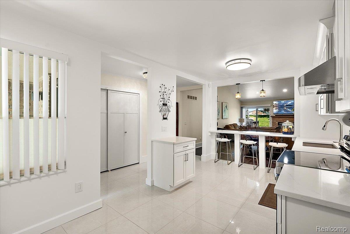552 Tennyson Rochester, MI 48307 - Photo 14 of 36 White kitchen featuring tile flooring, white cabinetry, a built-in breakfast bar, stainless steel appliances, and an open pass-through to an adjacent living area
