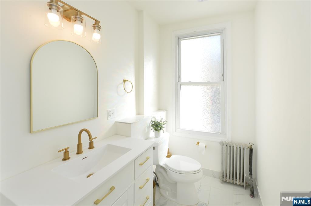 209 Adams Street, Unit 5 Hoboken, NJ 07030 - Photo 4 of 15 a bathroom with a toilet a sink a mirror and a window