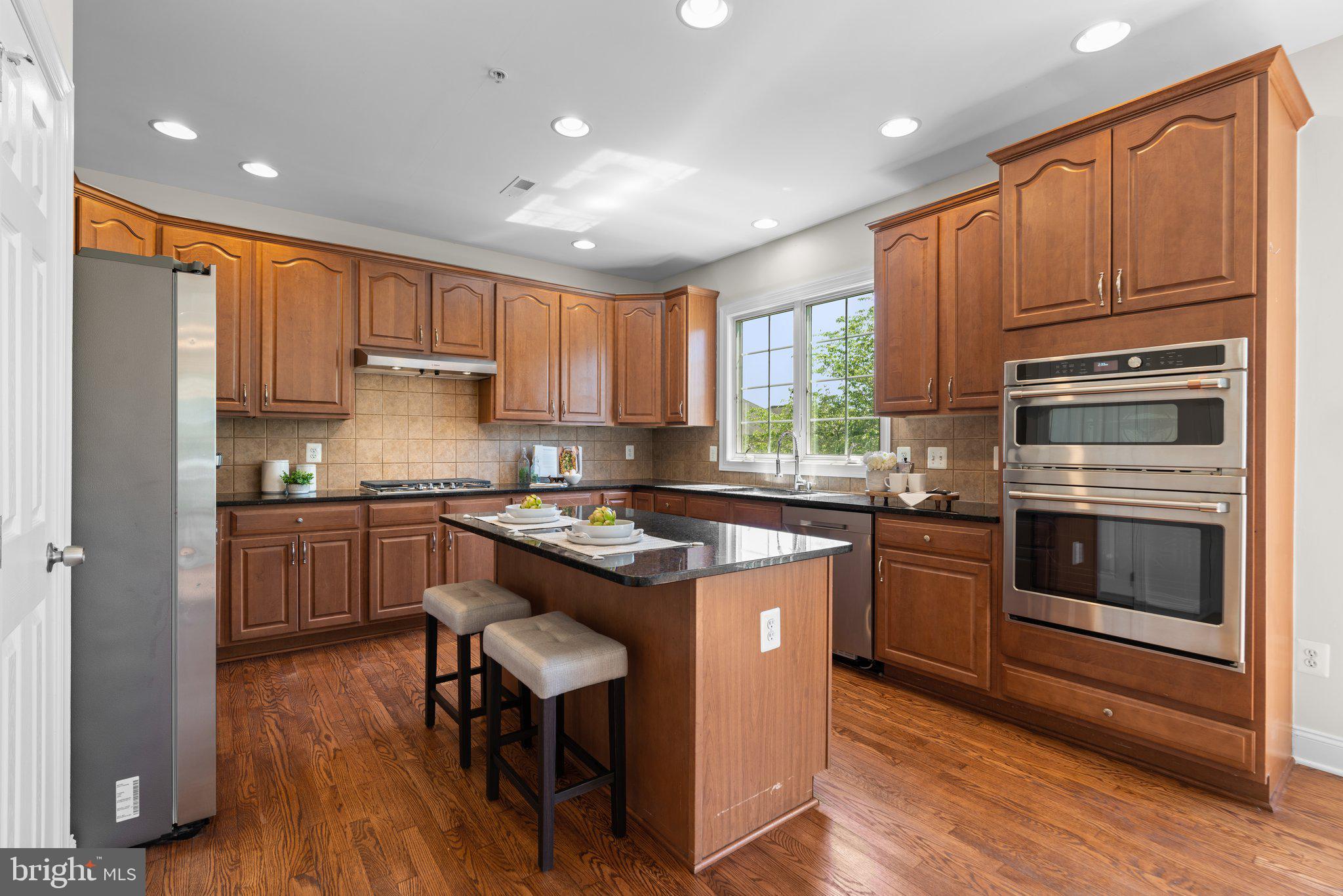 22104 Ginger Tree Way Clarksburg, MD 20871 - Photo 10 of 57 a kitchen with kitchen island granite countertop wooden floors stainless steel appliances and white cabinets
