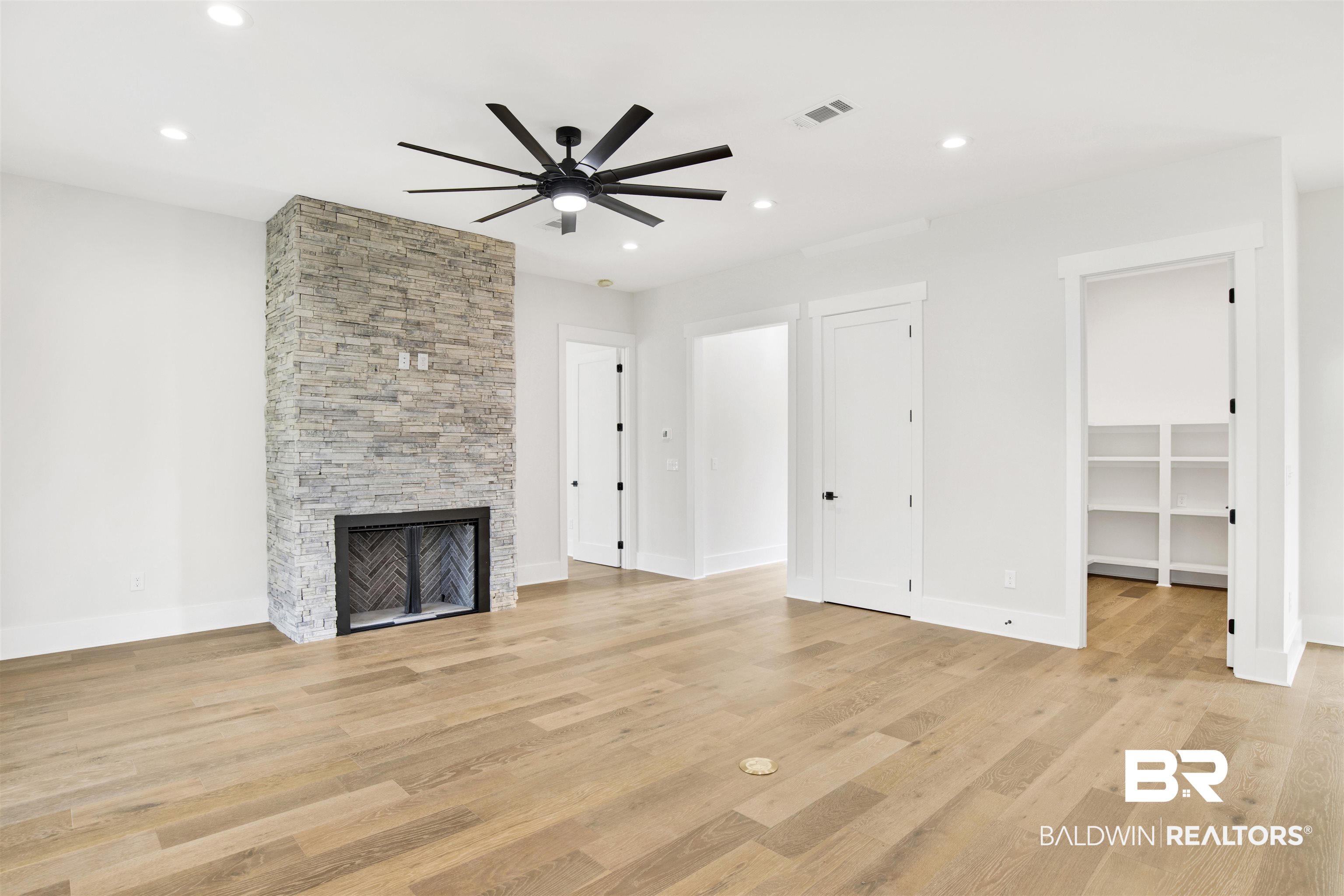 31545 River Road Orange Beach, AL 36561 - Photo 11 of 59 Unfurnished living room with engineered wood flooring, stone fireplace, ceiling fan--overlooking covered patio and summer kitchen