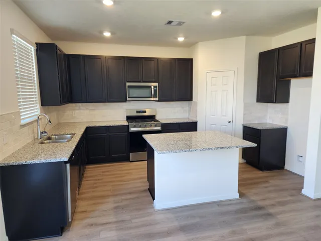 a kitchen with kitchen island granite countertop a stove top oven a sink dishwasher and a refrigerator with wooden floor