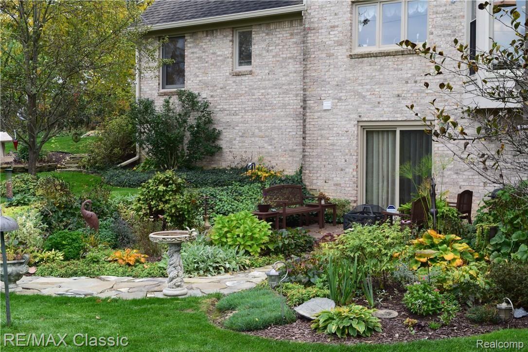 12825 Larkins Road Brighton, MI 48114 - Photo 37 of 39 Rear elevation features lush gardens and a charming stamped concrete patio.