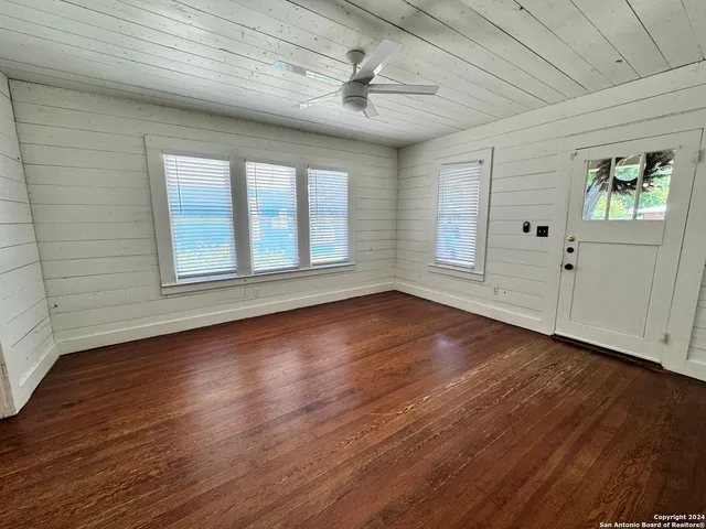 an empty room with wooden floor chandelier fan and windows