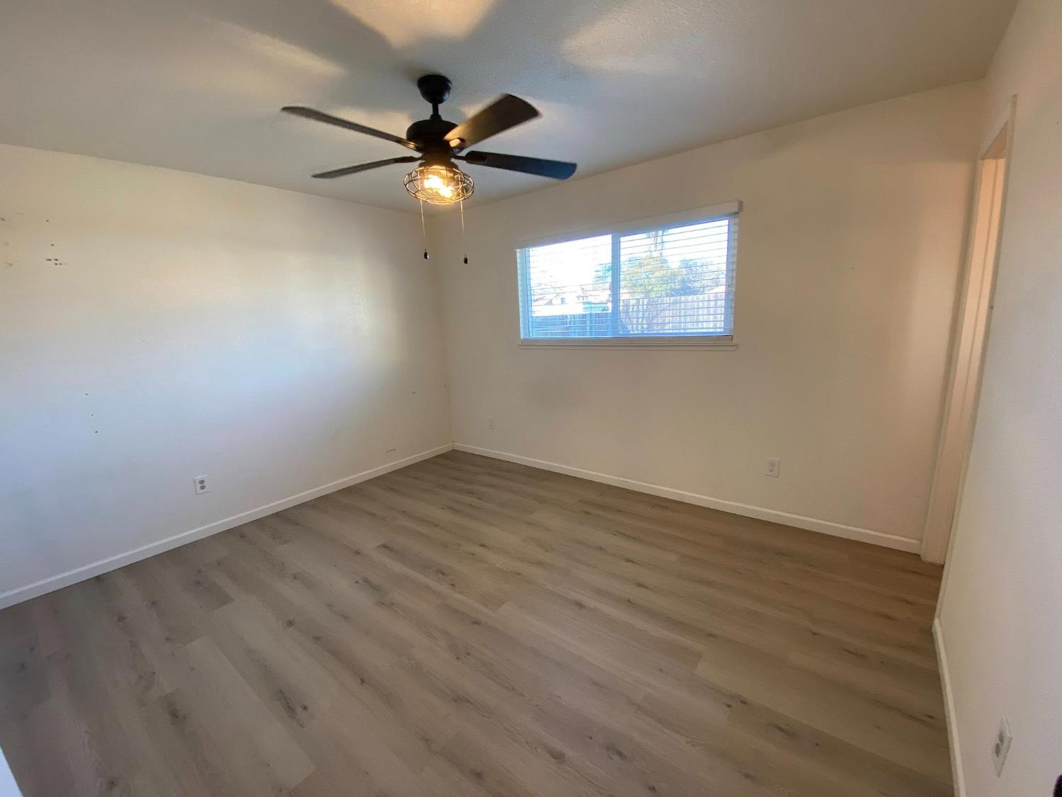 1201 Chateaugay Drive Modesto, CA 95356 - Photo 14 of 32 an empty room with wooden floor fan and windows