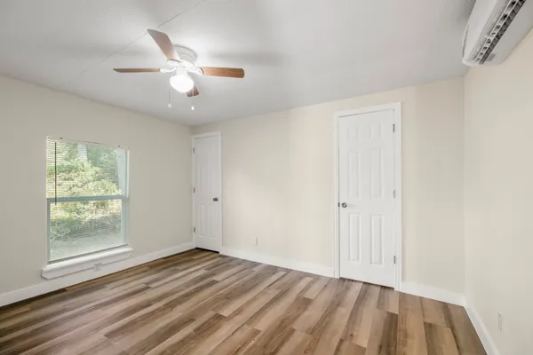 an empty room with wooden floor fan and windows