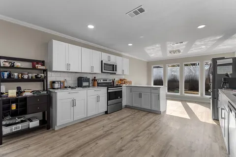 a kitchen with stainless steel appliances granite countertop a stove top oven a sink dishwasher a refrigerator and white cabinets with wooden floor