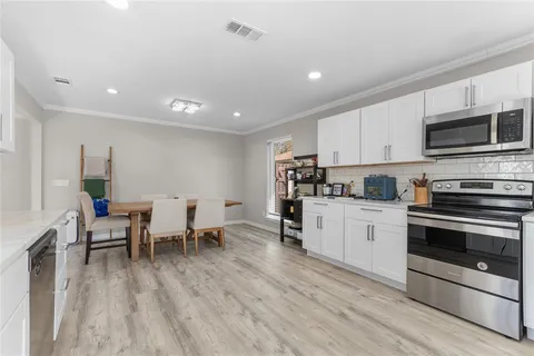 a kitchen with stainless steel appliances a stove top oven a sink dishwasher a dining table and chairs with wooden floor