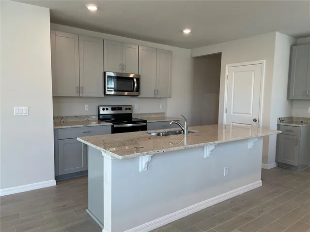 a kitchen with stainless steel appliances a sink a stove a microwave a refrigerator a sink and cabinets