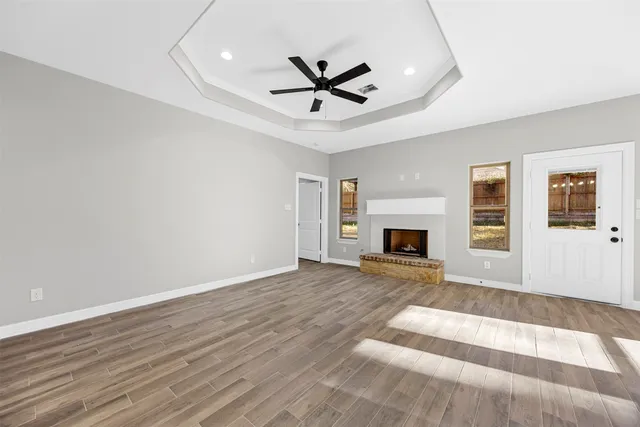 a view of a livingroom with a fireplace a ceiling fan and wooden floor