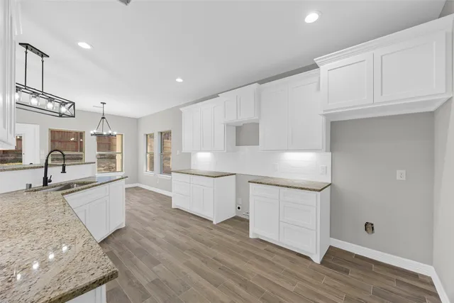 a large white kitchen with granite countertop a stove a sink and white cabinets with wooden floor