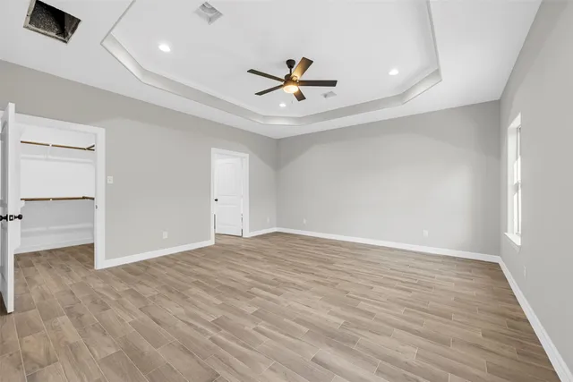 an empty room with wooden floor a ceiling fan and windows