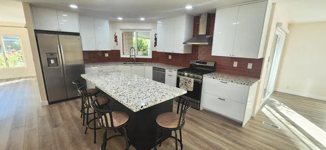 a kitchen with stainless steel appliances granite countertop a kitchen island a stove a refrigerator a sink a dining table and chairs with wooden floor