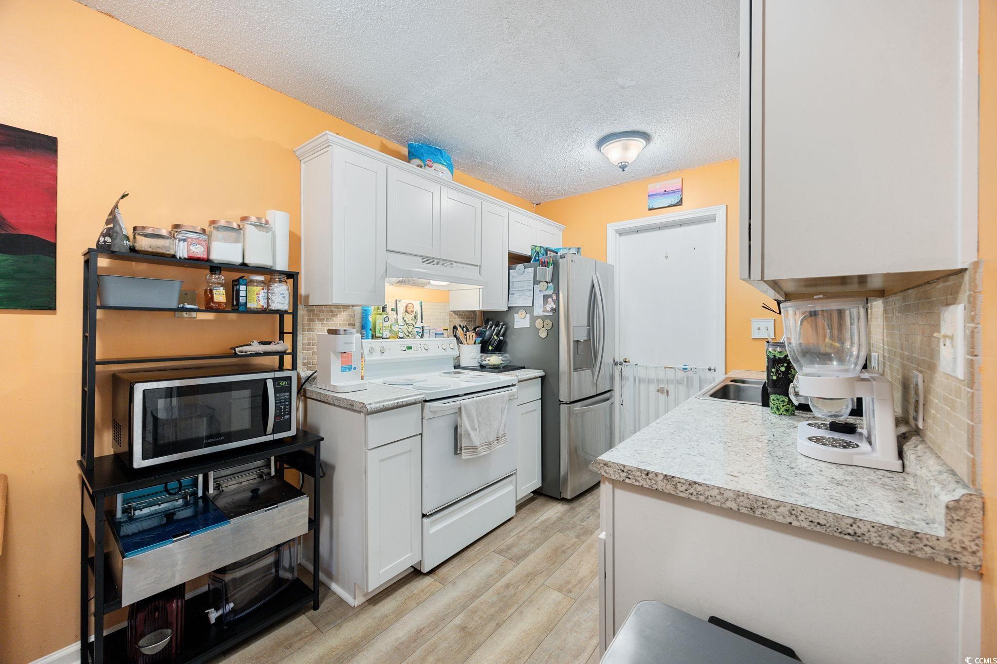 755 Burcale Road, Unit F4 Myrtle Beach, SC 29579 - Photo 12 of 30 Kitchen with white electric range, a textured ceiling, stainless steel microwave, white cabinets, and light wood finished floors