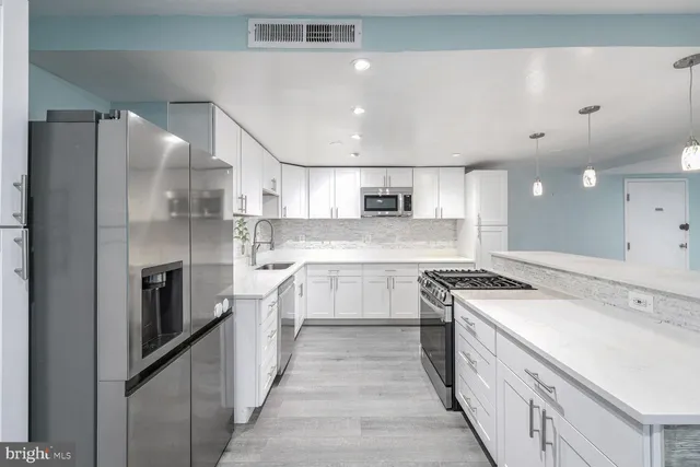 a large kitchen with a large counter top a sink stainless steel appliances and cabinets